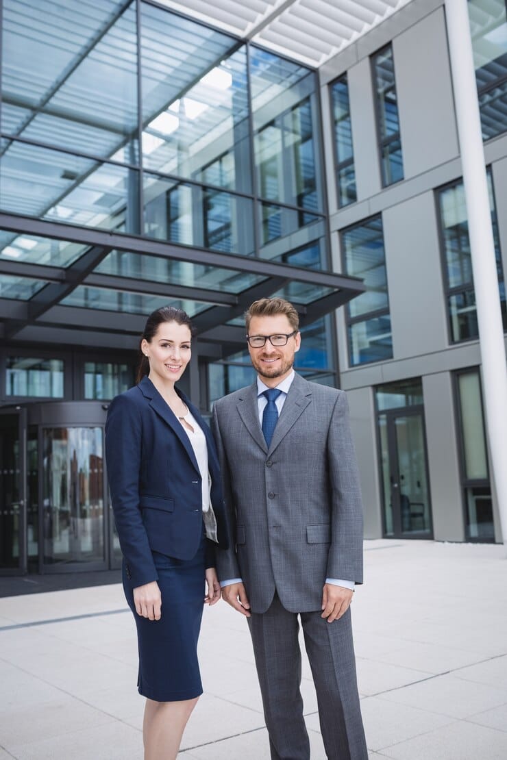 confident-businessman-with-colleague-standing-outside-office-building_107420-84730